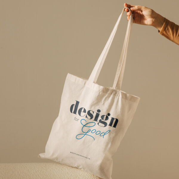 A person holding a canvas tote bag with the text "design for good" printed on it.