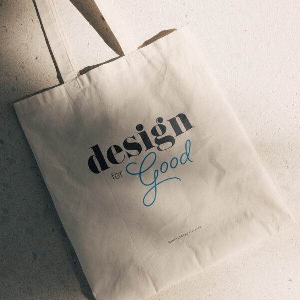 A Design for Good Sustainable Tote Bag rests on a textured surface, casting a soft shadow.