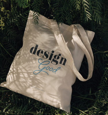 A Design for Good sustainable tote bag, resting among green leaves.