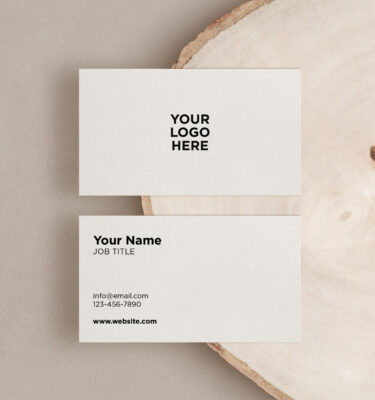 Two business cards on a wood surface, one face-up and one face-down. The face-up card displays placeholders for a logo, name, job title, email, phone number, and website, perfect for your next promotion.